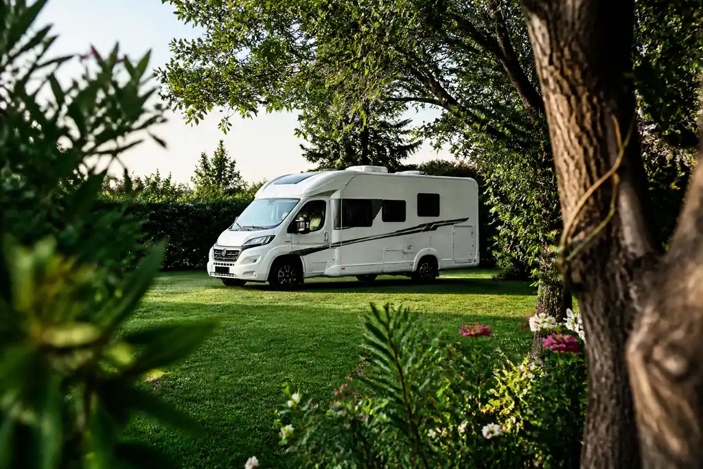 Camping car blanc stationne dans un jardin verdoyant